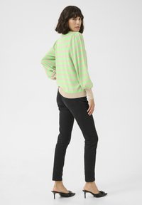 Maglione a righe in verde chiaro e beige, con maniche a sbuffo e scollatura rotonda. Abbinato a pantaloni neri slim-fit e mule nere con tacco.