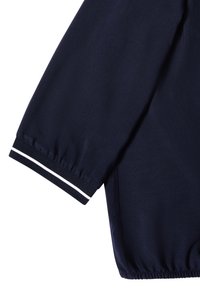 Manche de veste bleu marine avec poignet élastique et détail double bande blanche sur fond blanc.
