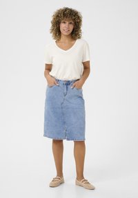 Leren rok in lichtblauw met een rechte snit, voorzakken en een knoopsluiting. Gepaard met een crème V-hals T-shirt en beige schoenen.