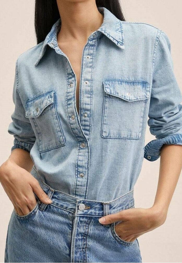 Chemise en denim bleu clair à manches longues, boutonnée à l'avant, avec deux poches poitrine et une coupe décontractée. Portée avec un jean en denim taille haute.