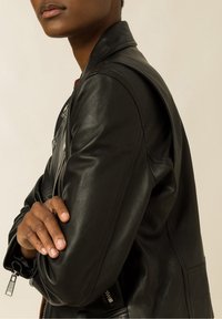 Svart läderjacka med en mjuk textur, silverdragkedjedetalj och en figursydd silhuett. Har en ståkrage och sidofickor.