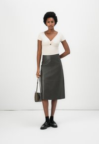 Lys beige tilpasset topp med et vridd frontdetalj, sammen med en mørkegrønn skinn midi skjørt. Svarte sko og en liten veske fullfører antrekket.