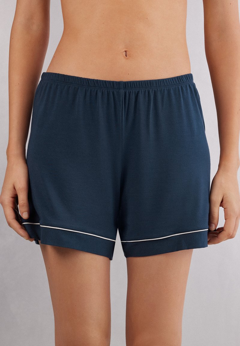 Marineblauwe comfortabele shorts van zachte stof, met een elastische tailleband en een witte bies langs de zoom. Glad textuur.