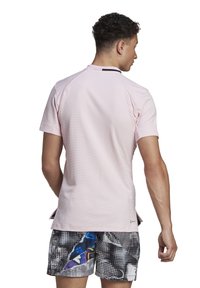 T-shirt de sport à manches courtes rose, avec un motif texturé, présentant des accents noirs au niveau de l'encolure arrière et des fentes sur les côtés pour améliorer la mobilité.