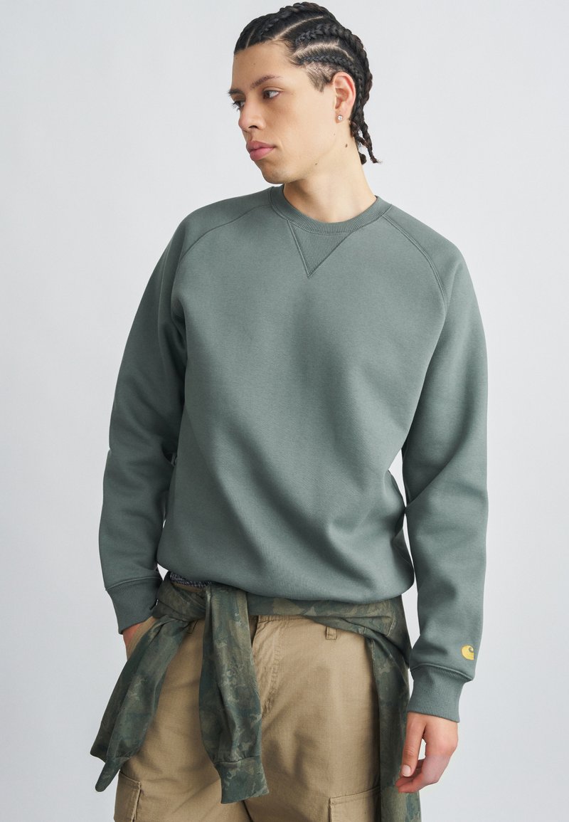 Pilko žalios spalvos džemperis su ribotu apvaliu kaklu ir raglano rankovėmis. Derinamas su smėlio spalvos kelnių su kišenėmis modeliu ir žalia kamufliažine medžiaga, surišta aplink juosmenį.