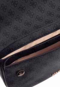 Sac à main noir texturé avec motif embossé, doublure beige et fermeture à pression magnétique. Comprend deux compartiments intérieurs.