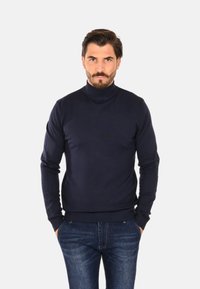 Maglione a collo alto blu navy realizzato in tessuto a maglia liscia. Design aderente con collo e polsini a coste, abbinato a jeans scuri in denim.