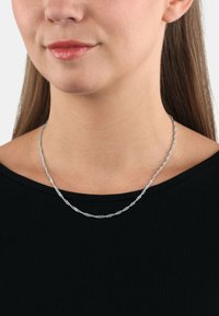 Collana a catena di argento attorcigliata indossata su una maglia nera, caratterizzata da una texture delicata e un leggero lucido, posata sulla clavicola.