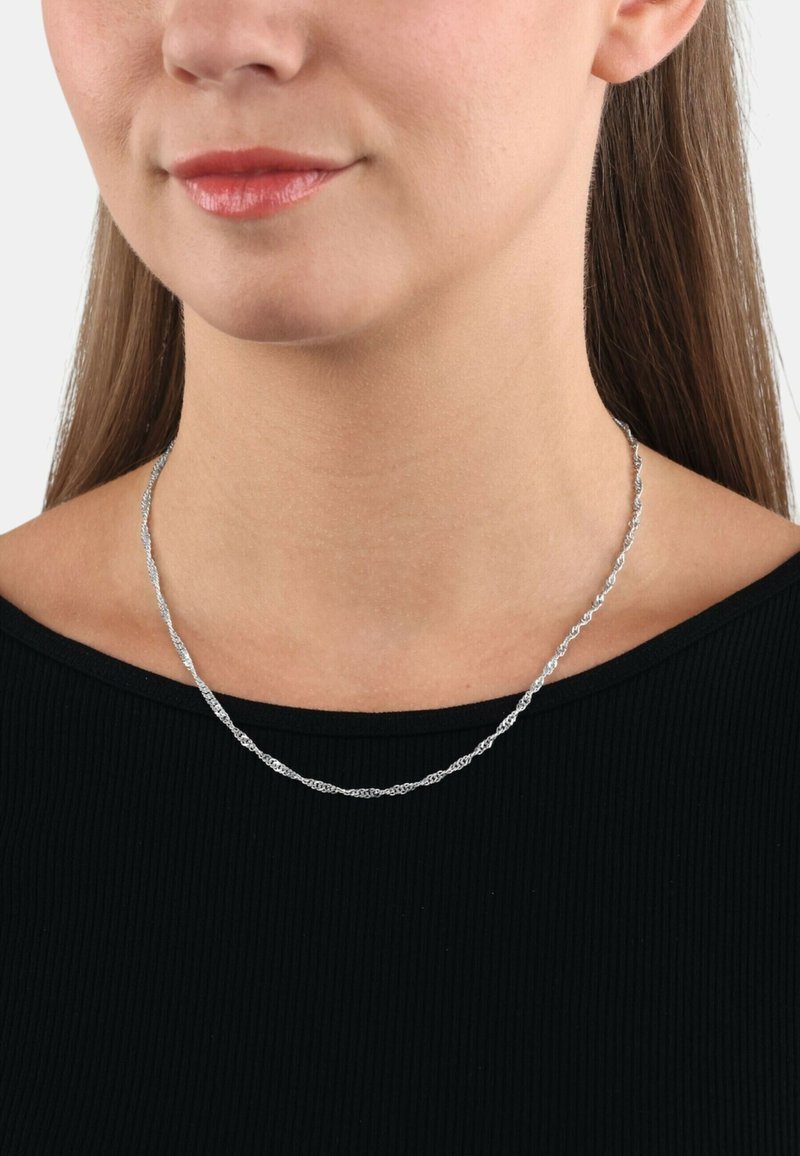 Collana a catena di argento attorcigliata indossata su una maglia nera, caratterizzata da una texture delicata e un leggero lucido, posata sulla clavicola.