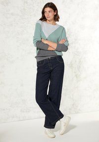 Lätt, texturerad tröja i teal och grå med ett geometriskt mönster, kombinerad med mörkblå vida jeans och vita sneakers.
