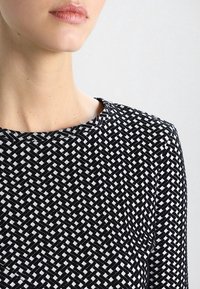 Haut à motifs noir et blanc avec un col rond et un tissu tissé texturé, présentant un design géométrique.