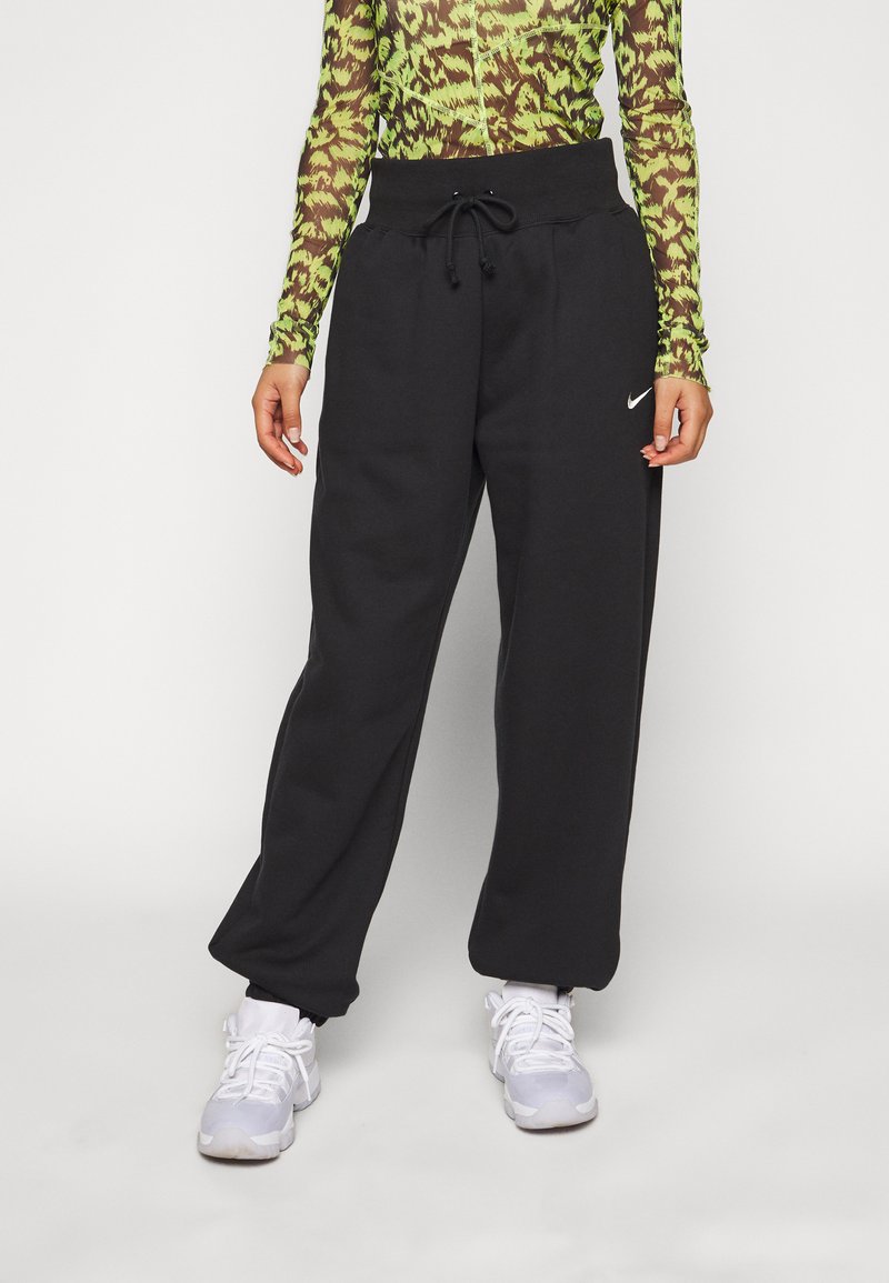 Schwarze Sweatpants mit einem verstellbaren Bund, die eine lockere Passform und Seitentaschen bieten. Kombiniert mit weißen Sportschuhen.