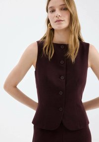 Vesta bordo fără mâneci, cu un design mulat, cu gât înalt și șase nasturi frontali pentru închidere. Textură netedă a materialului, croială ajustată.