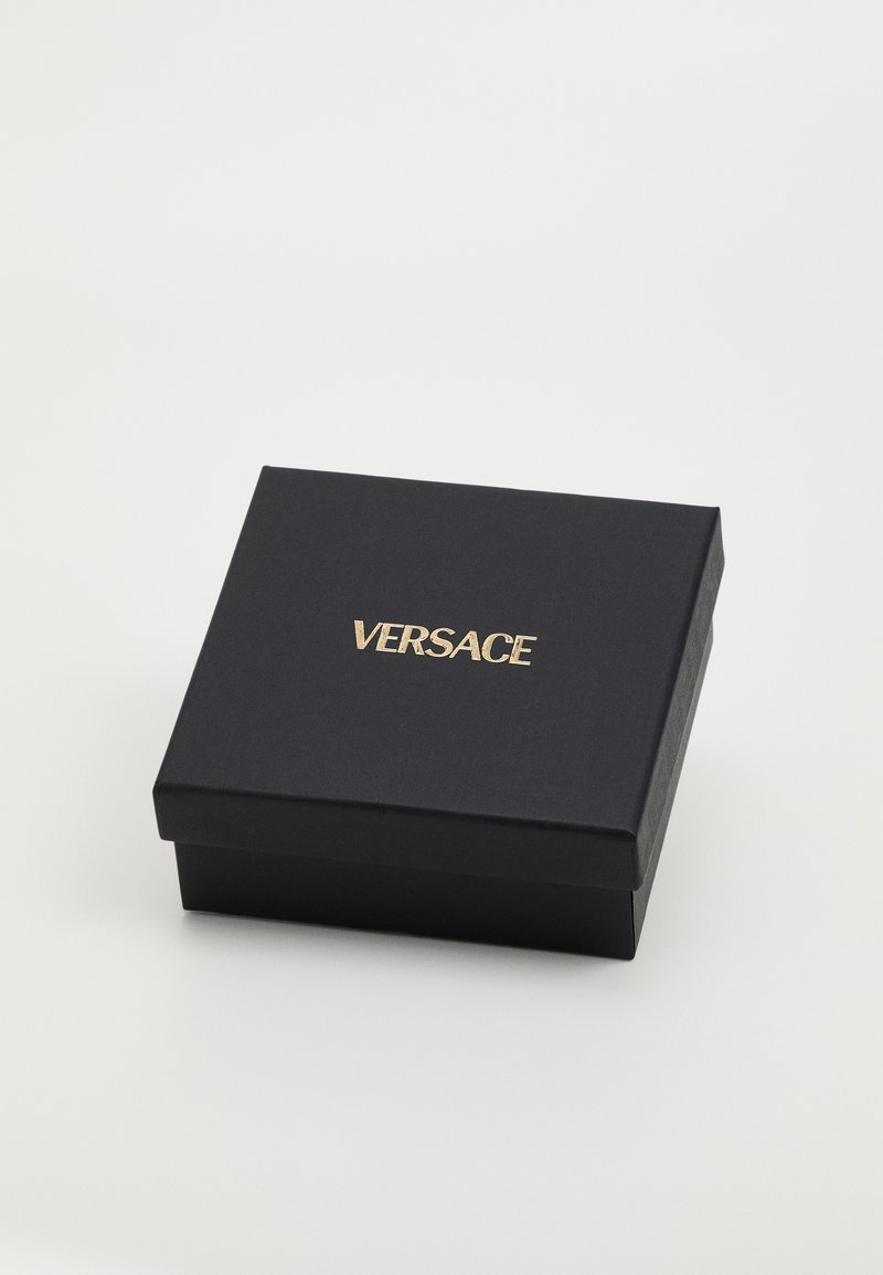 Caja de regalo negra con un acabado texturizado, que presenta un logo dorado de "VERSACE" en la tapa. De forma cuadrada, con una construcción robusta.