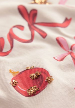 Tessuto di cotone con una grafica di una mela rossa decorata con paillettes dorate, accenti di nastri rosa e rossi, e uno sfondo bianco texturizzato.