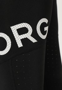 Czarne legginsy sportowe z białymi kropkowanymi napisami. Wykonane z oddychającego materiału z małymi perforacjami dla wentylacji. Zaprojektowane z myślą o wydajności.