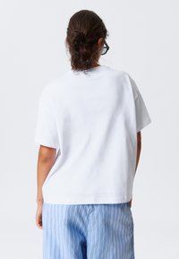 T-shirt blanc à manches courtes avec une coupe décontractée et un col rond, associé à un pantalon rayé bleu clair. Texture en coton lisse.