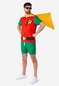 Crvena i zelena majica s kratkim rukavima ima dizajn u stilu stripa s velikim slovom "R" i crnim akcentima. Uparena je sa zelenim šortsevima i bijelim tenisicama.