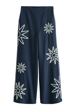 Tmavomodré nohavice s širokými nohavicami, zdobené bielou vyšívanou slnečnou potlačou rozptýlenou na prednej strane a bokoch, s elastickým pásom.