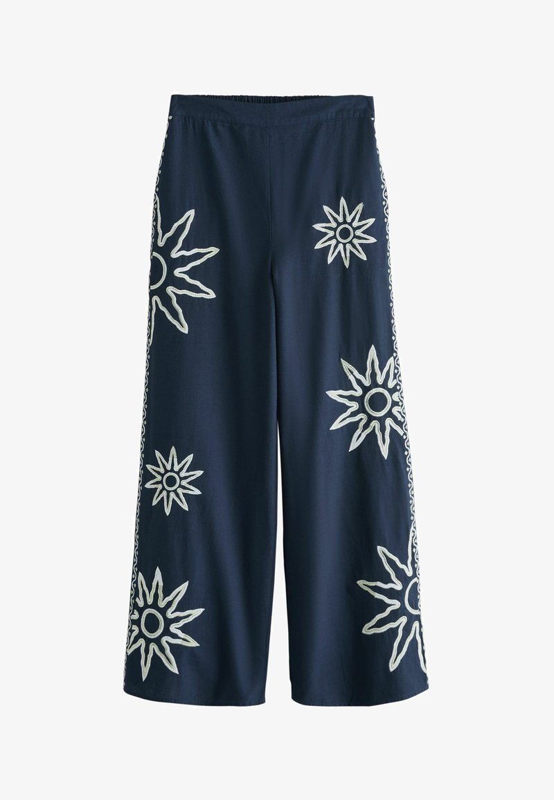Pantalon large bleu marine avec des motifs de soleil blancs brodés dispersés à l'avant et sur les côtés, avec une ceinture élastique.