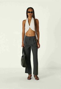 Top branco sem mangas com frente atada, calças cinzas de cintura alta, bolsa oversized preta e sandálias pretas com tiras.