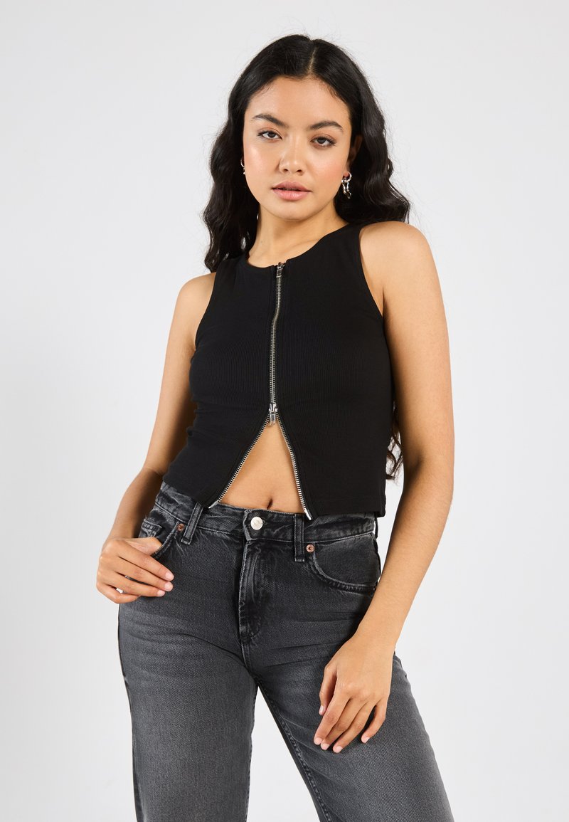 Čierny rebrovaný crop top s predným zipsom a okrúhlym výstrihom. S duom so svetlo vyblednutými čiernymi džínsami s vysokým pásom.