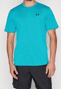 Turkos idrottströja med geometriskt mönster, korta ärmar och rundad krage. Företagslogotyp i svart på vänster bröstparti.