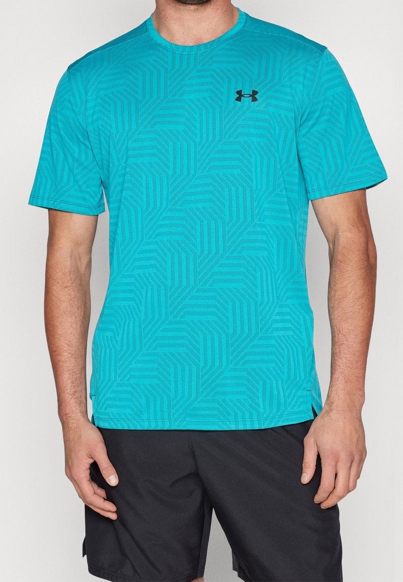 Turkos idrottströja med geometriskt mönster, korta ärmar och rundad krage. Företagslogotyp i svart på vänster bröstparti.