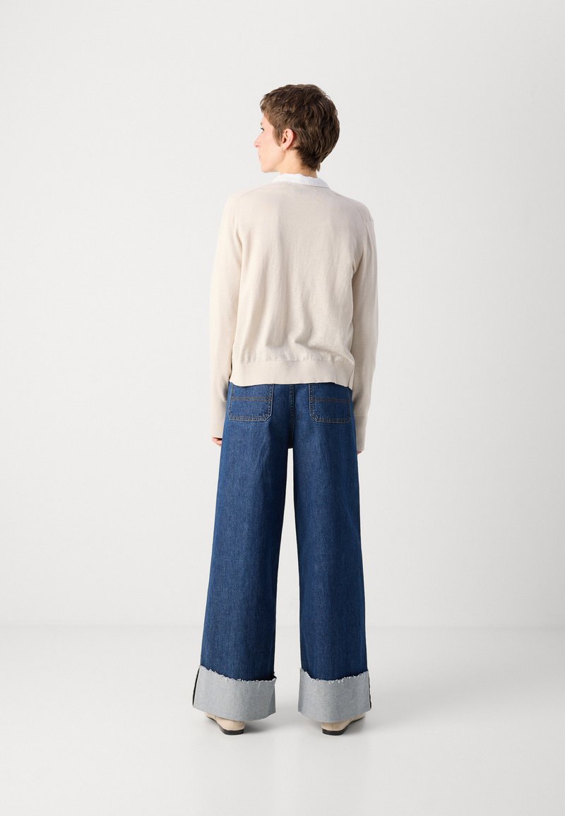 Helles beiges gestricktes Sweatshirt mit Rundhalsausschnitt, kombiniert mit weiten blauen Denim-Jeans mit ausgefranstem hellblauem Saum und Gesäßtaschen.