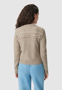 Maglione beige lavorato a maglia con schiena texturizzata e rifiniture in pizzo, bordo a costine. Abbinato a pantaloni in denim blu chiaro.