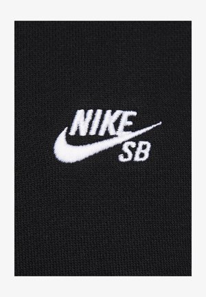 Svart stoff med teksturert strikk, med hvit brodert "NIKE SB"-logo og swoosh, som viser kontrast i farge og merkevare.