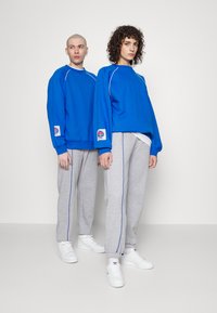 Felpe blu oversize con dettagli bianchi, abbinate a pantaloni della tuta grigi con piping blu. Sneakers bianche completano gli outfit.