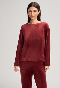 Burgunderfarbene Velour-Lounge-Set bestehend aus einem lockeren Langarmoberteil und passenden Hosen mit einer glatten Textur und minimalen Hardware-Akzenten.