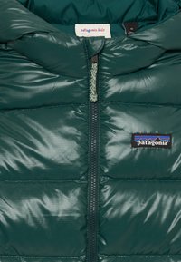 Patagonia kinder pufferjack in donkergroen, met een ritssluiting aan de voorkant, een gewatteerde textuur en een logo-opdruk op de borst. Gemaakt van polypropyleen.