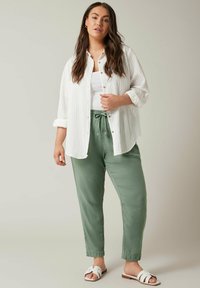 Witte overhemd met verticale strepen, gecombineerd met lichtgroene broek met koordjes. Sandalen hebben brede banden en een platte zool.