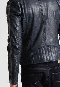 Námořnická modrá kožená motocyklová bunda s žebrovanými akcenty, zipovými stranami a texturovanými panely. Přiléhavý střih s kratším designem.