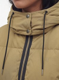 Gros plan d'une veste matelassée marron avec une fermeture éclair noire, un col montant avec deux boutons-pression métalliques, et des cordons noirs avec des embouts argentés.