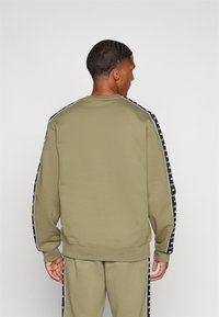 Sudadera verde oliva de manga larga, con rayas laterales negras adornadas con texto blanco. Tejido suave y puños y dobladillo acanalados.