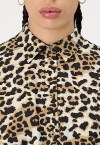 Camicia con motivo leopardato, colletto, tonalità beige e nere, dotata di chiusura con bottoni e tessuto texturizzato.
