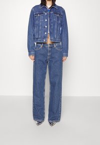 Džínová bunda s knoflíkovým zapínáním a dvěma kapsami na prsou, doplněná širokými džínami s volným střihem. Obě v středně modré barvě s ležérním střihem.