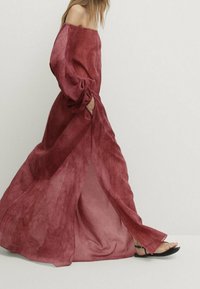 Robe maxi décolletée dans un rouge profond, avec des manches longues, une silhouette fluide et des poches latérales. Fabriquée en tissu doux et léger.