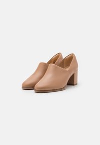 Chaussures à talons blocs en cuir beige avec bout fermé, texture lisse et design minimaliste. Elles disposent d'un talon robuste pour plus de stabilité.
