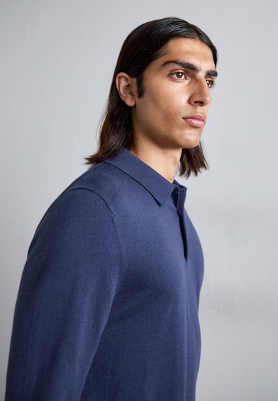 Navy blue long-sleeve polo shirt with a soft texture, featuring a classic collar and a subtle placket. Minimalist design, fitted silhouette.