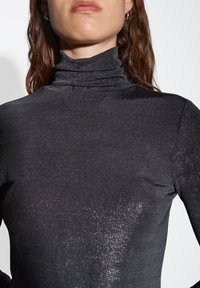 Maglione aderente nero a collo alto con una sottile lucentezza metallica, caratterizzato da un tessuto a coste testurizzato e un design con collo alto.