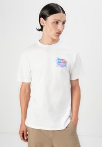 Biały bawełniany t-shirt z krótkimi rękawami, z kolorowym logo graficznym na lewej stronie klatki piersiowej. Wzór zawiera palmy i tekst.