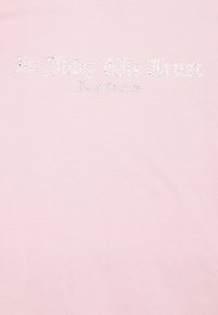 Růžové bavlněné tričko s krystalovými ozdobami, které píší "Juicy Couture" kurzívou, s hladkým povrchem a uvolněným střihem.