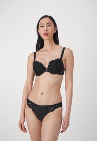 Set di lingerie nera con reggiseno con pizzo e scollatura profonda, abbinato a slip con dettagli in pizzo. Tessuto morbido al tatto.