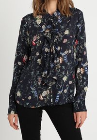 Blusa a maniche lunghe di un blu navy scuro, con un motivo floreale e uccelli, davanti arricciato e colletto con bottoni. Realizzata in tessuto morbido.