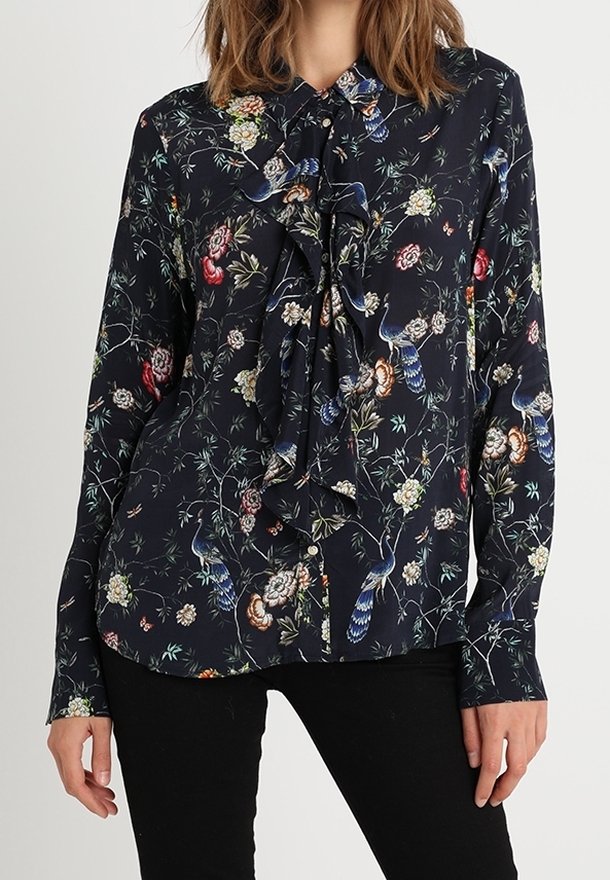 Blusa a maniche lunghe di un blu navy scuro, con un motivo floreale e uccelli, davanti arricciato e colletto con bottoni. Realizzata in tessuto morbido.