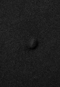 Czarna filcowa tkanina o miękkiej, fakturowanej powierzchni z wyraźnym centralnym guzikiem. Okrągły kształt o jednolitym wyglądzie.